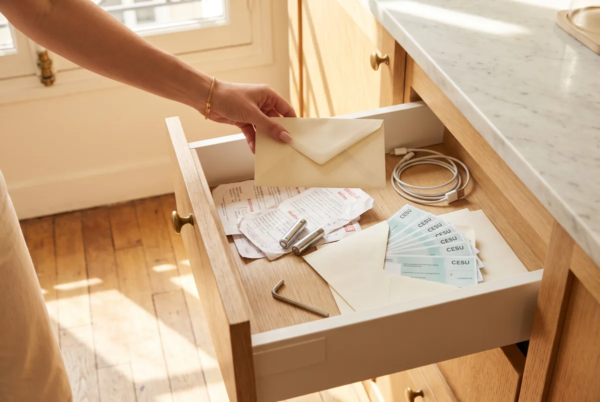 Payer votre femme de ménage en CESU : où utiliser vos chèques, et ce qu'ils valent vraiment 1 Tiroir de cuisine ouvert : enveloppes de chèques CESU au milieu des menus et des piles